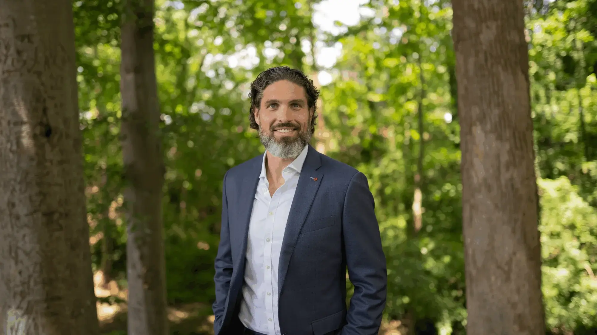 Chris Carsten in a navy suit, standing among tall trees